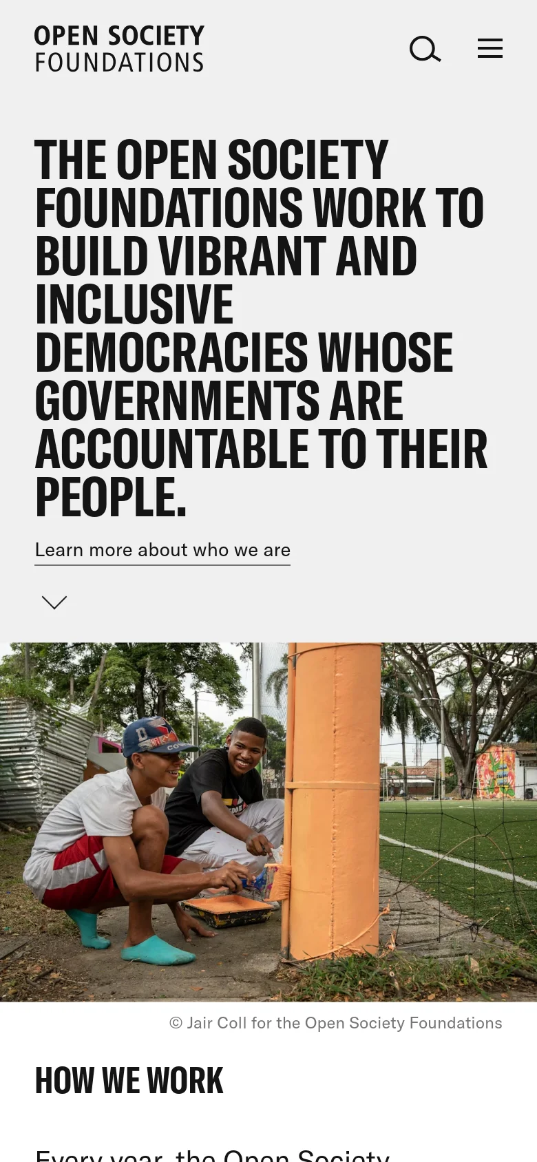 The mobile version uses a stacked layout where the large bold headline and 'Learn more about who we are' link appear first on a light background, followed by the photograph of the two men. The header is simplified with the logo, a search icon, and a hamburger menu positioned at the top.