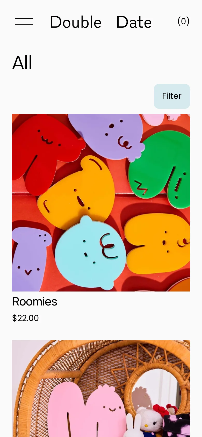 The mobile version presents a simplified view with a large 'All' heading and a prominent 'Filter' button. The product grid shifts to a single-column layout, focusing on large, vibrant imagery of colorful character-shaped items like 'Roomies' with their respective prices listed below.
