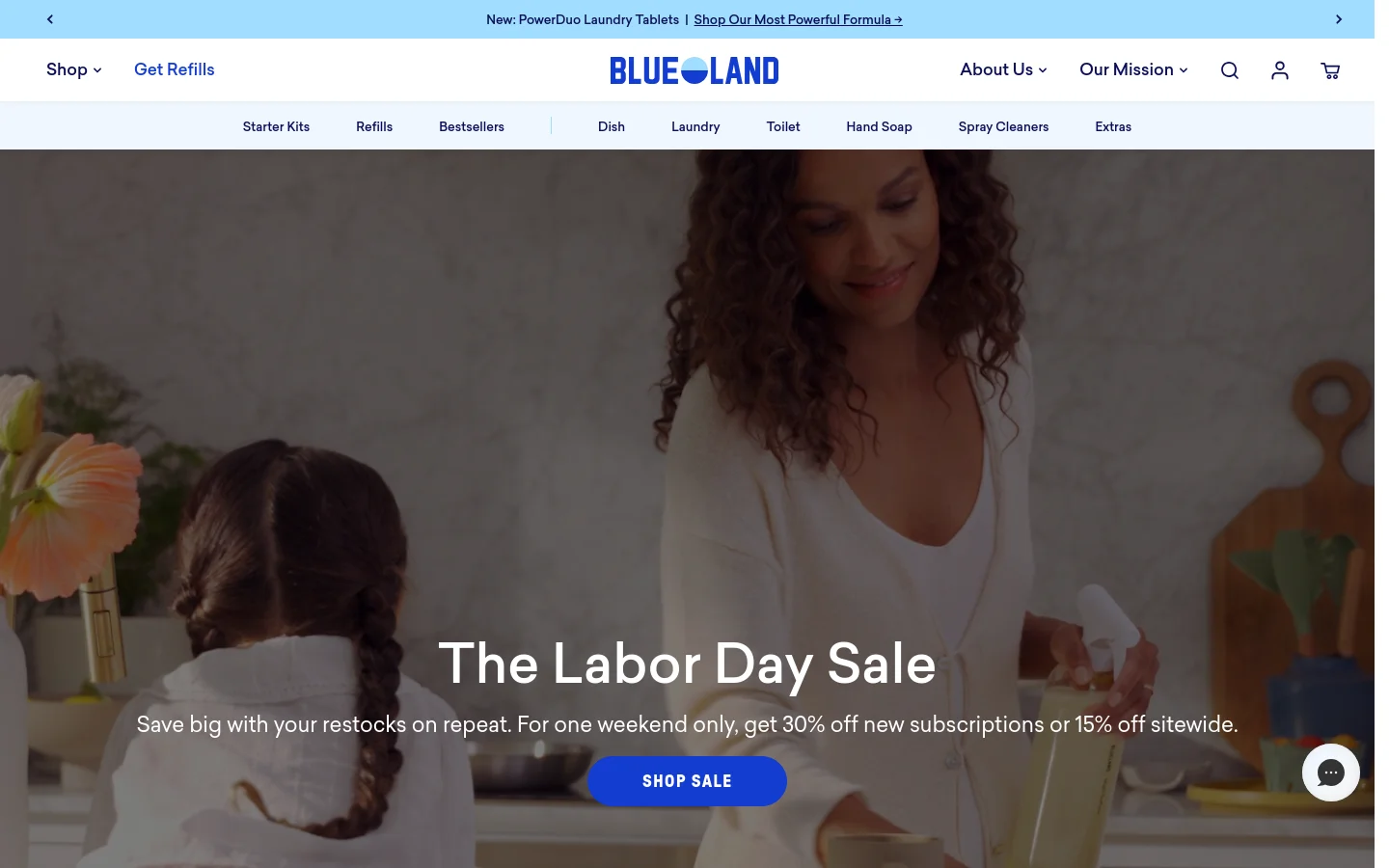 The Blueland homepage features a large hero image of a woman in a kitchen with a Labor Day Sale announcement and a blue 'SHOP SALE' button. A white navigation bar at the top includes the brand logo, shop categories like Starter Kits and Refills, and utility icons for search, account, and cart. A light blue announcement bar sits at the very top.