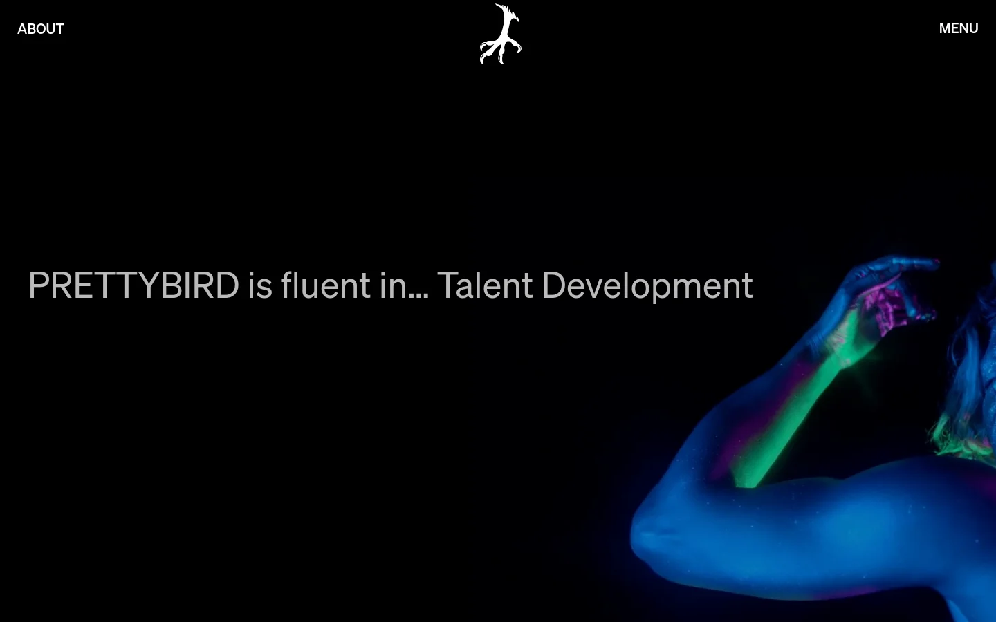 The desktop About page features a dark, minimalist design with a large hero image of a person's torso and arm illuminated in neon blue and green light against a black background. Large white text overlays the image, stating 'PRETTYBIRD is fluent in... Talent Development'. The header includes the word 'ABOUT' on the left, a white bird logo in the center, and 'MENU' on the right.