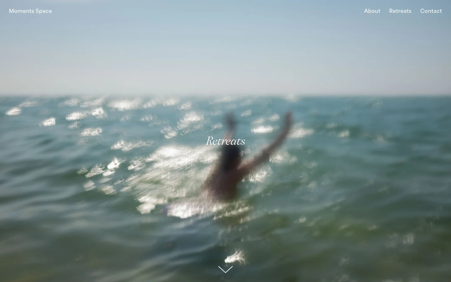 The desktop version features a minimalist design with a large, blurred hero image of a person in the ocean and the title 'Retreats' in white serif text. A navigation menu with links for About, Retreats, and Contact is positioned at the top right against a light blue sky background. A downward arrow icon at the bottom center indicates more content below.