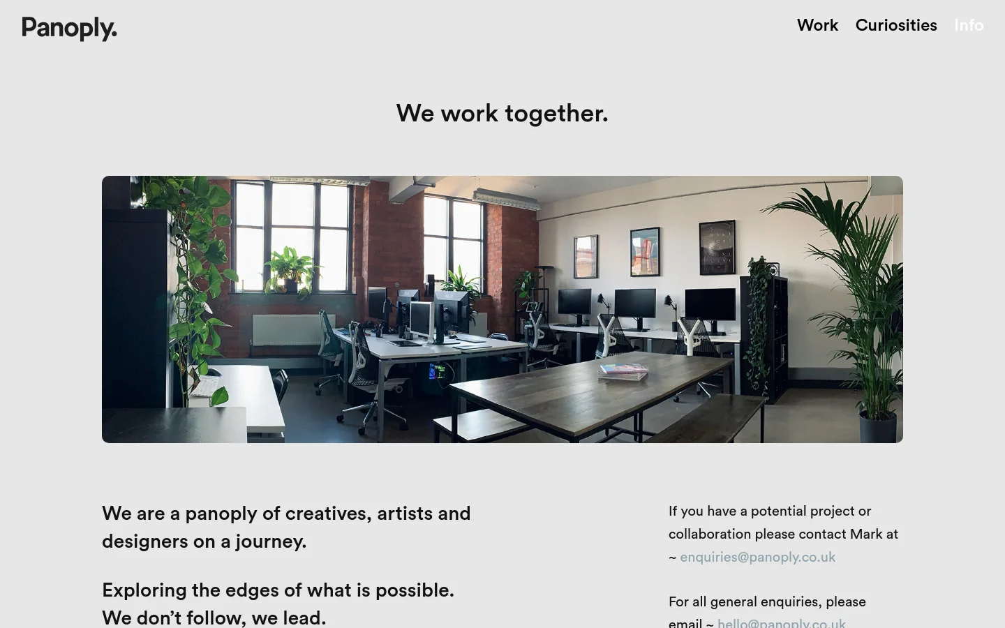 The desktop page features a minimalist light gray background with a top navigation bar containing the Panoply logo and links for Work, Curiosities, and Info. A large hero headline reads 'We work together' above a wide landscape photograph of a bright, modern studio office with desks, computers, and indoor plants. Below the image, text describes the creative team, followed by contact information and social media links.