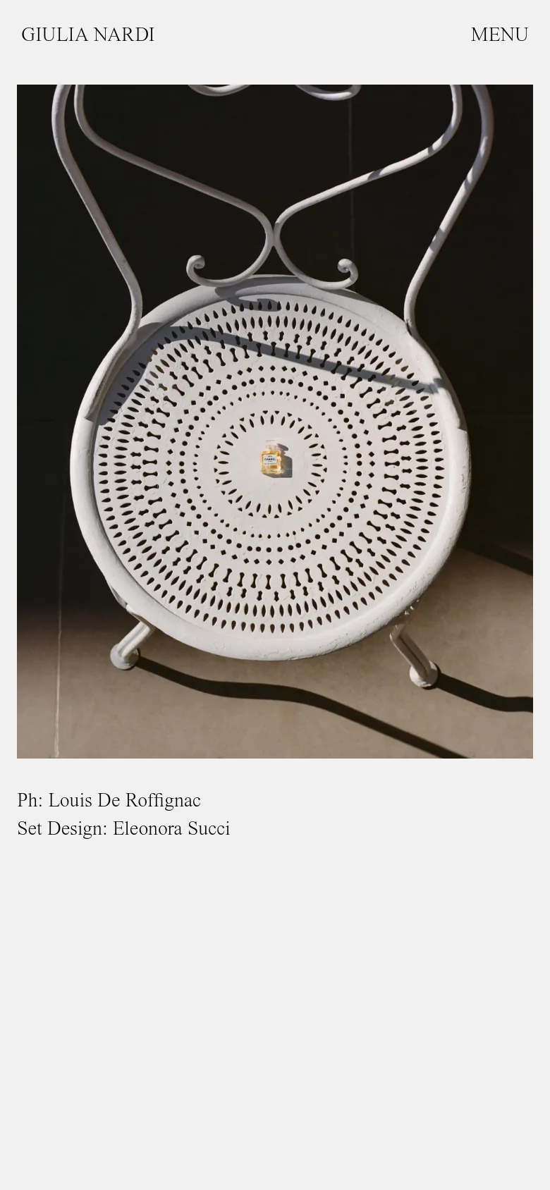 The mobile version presents a vertically stacked layout optimized for scrolling, focusing on the large editorial image of the white chair and gold product. The navigation is condensed into a 'MENU' button at the top right, while the brand name remains at the top left, maintaining the minimalist aesthetic with ample white space.