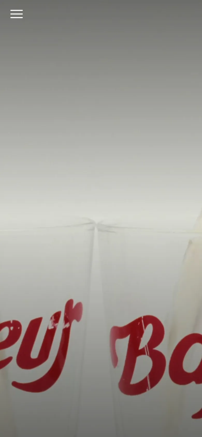The mobile version maintains the large hero image of beer being poured into branded glasses but simplifies the interface. The top navigation is replaced by a white hamburger menu icon on the left, focusing the visual attention entirely on the close-up imagery.
