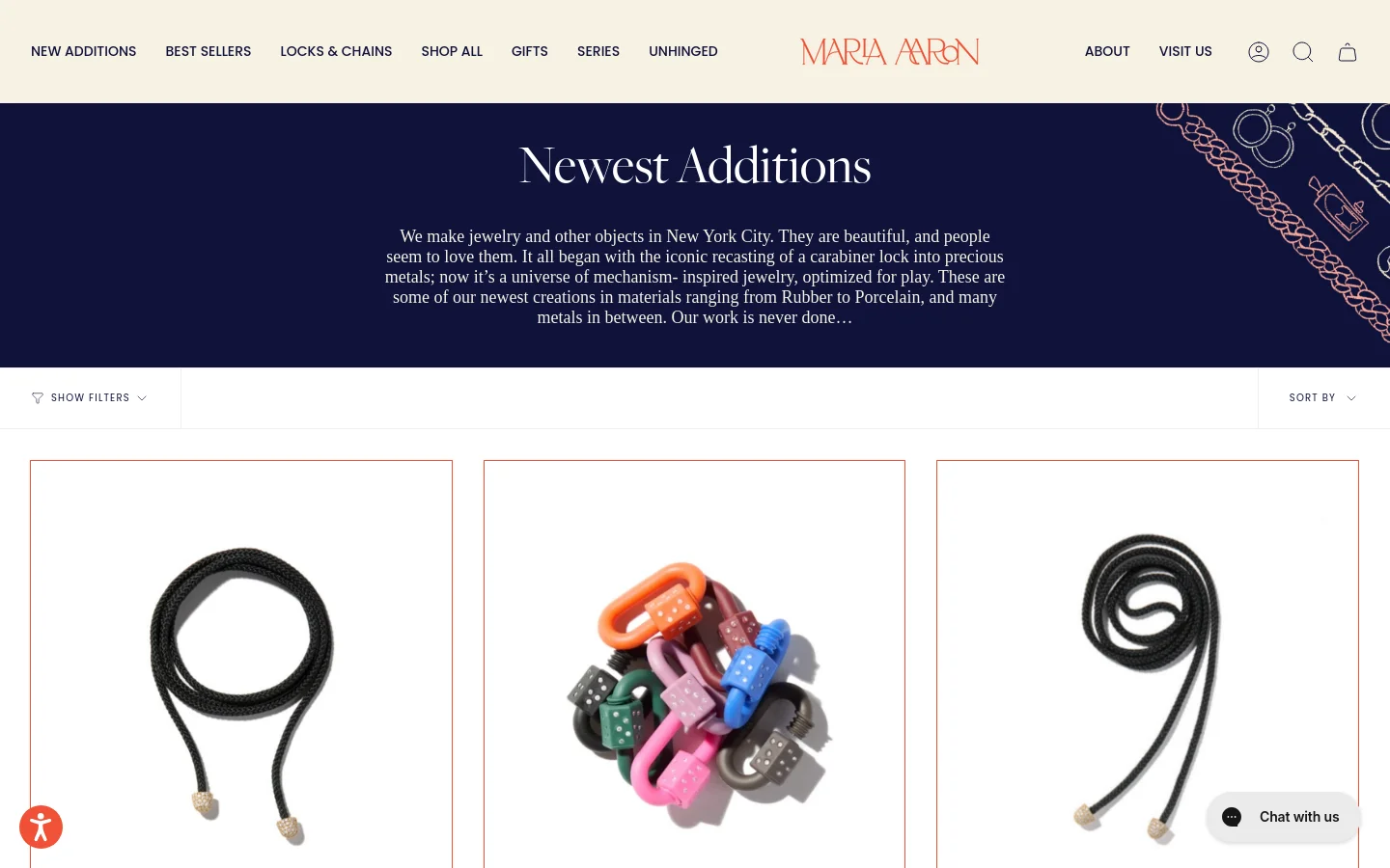 The desktop page features a dark navy hero section with the headline 'Newest Additions' and a descriptive paragraph about the brand's jewelry. Below, a white product grid displays jewelry items like black cord necklaces and colorful carabiner locks against a light background. A navigation bar at the top includes links for 'New Additions', 'Best Sellers', and 'Shop All', alongside a search icon and shopping bag.