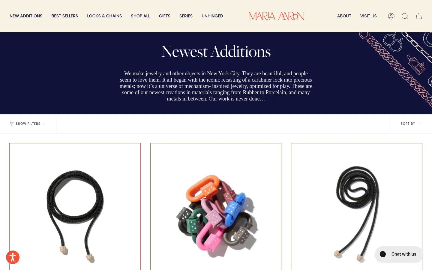 The desktop page features a dark navy hero section with the headline 'Newest Additions' and a descriptive paragraph about the brand's jewelry. Below, a white product grid displays jewelry items like black cord necklaces and colorful carabiner locks against a light background. A navigation bar at the top includes links for 'New Additions', 'Best Sellers', and 'Shop All', alongside a search icon and shopping bag.
