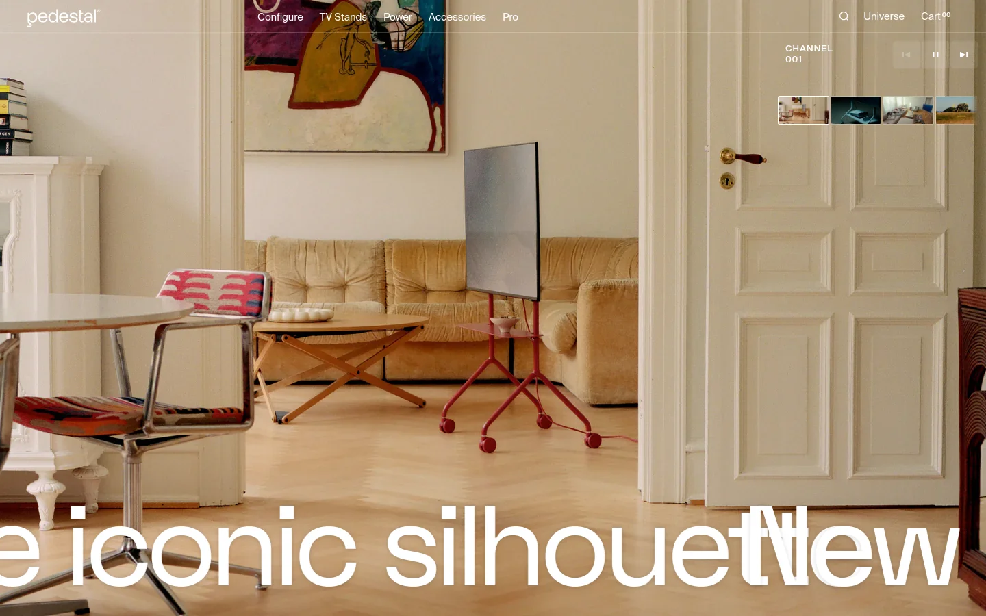 The desktop homepage features a large hero image of a minimalist living room with a red pedestal TV stand, overlaid with large white typography. A top navigation bar includes links for Configure, TV Stands, Power, Accessories, and Pro, alongside search, universe, and cart icons. Below the hero section, a grid of product categories like 'New colours' and 'Power Gems' is displayed with high-quality lifestyle photography.