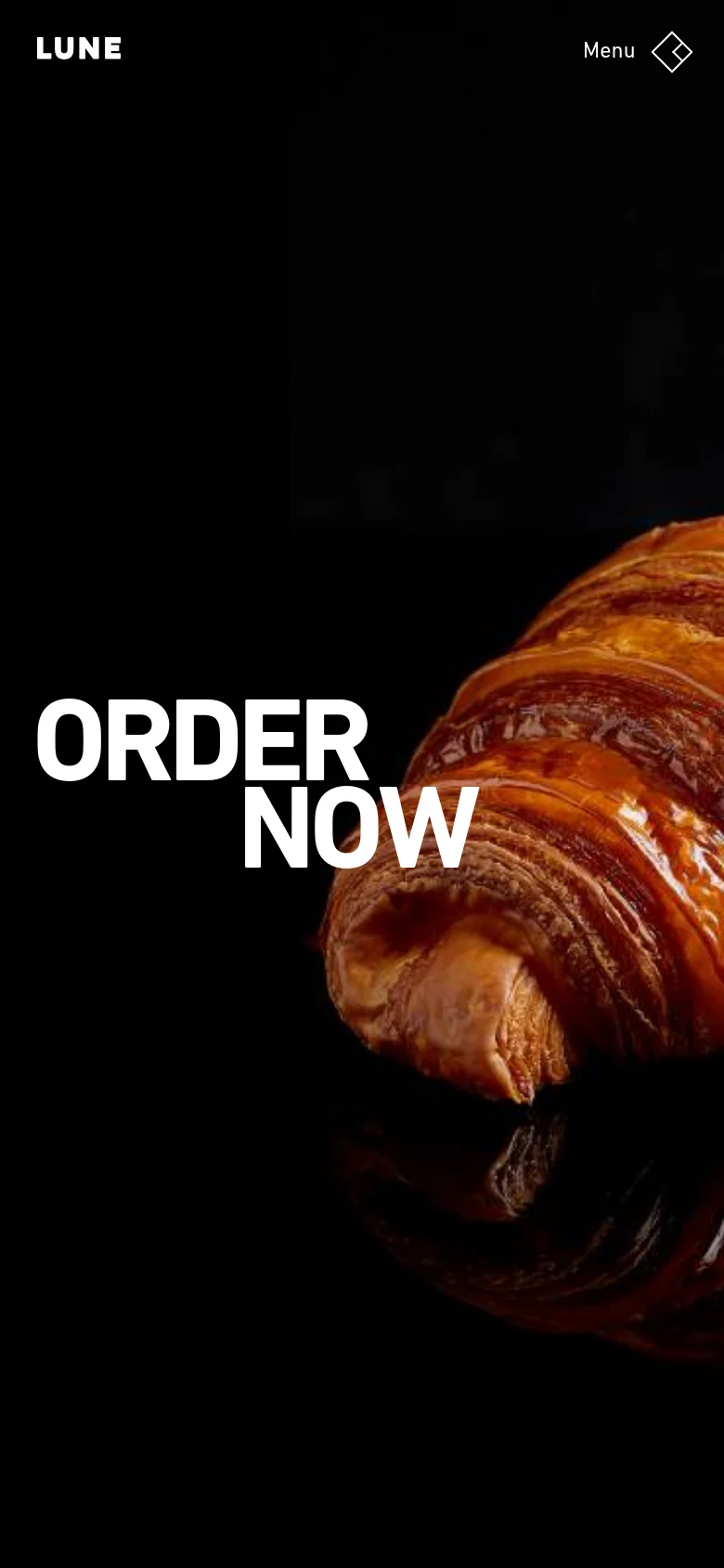 The mobile version maintains the dark aesthetic and hero imagery of the croissant, but the layout is condensed. The 'ORDER NOW' text is centered over the croissant, and the navigation is simplified into a 'Menu' button with a diamond icon in the top right corner.