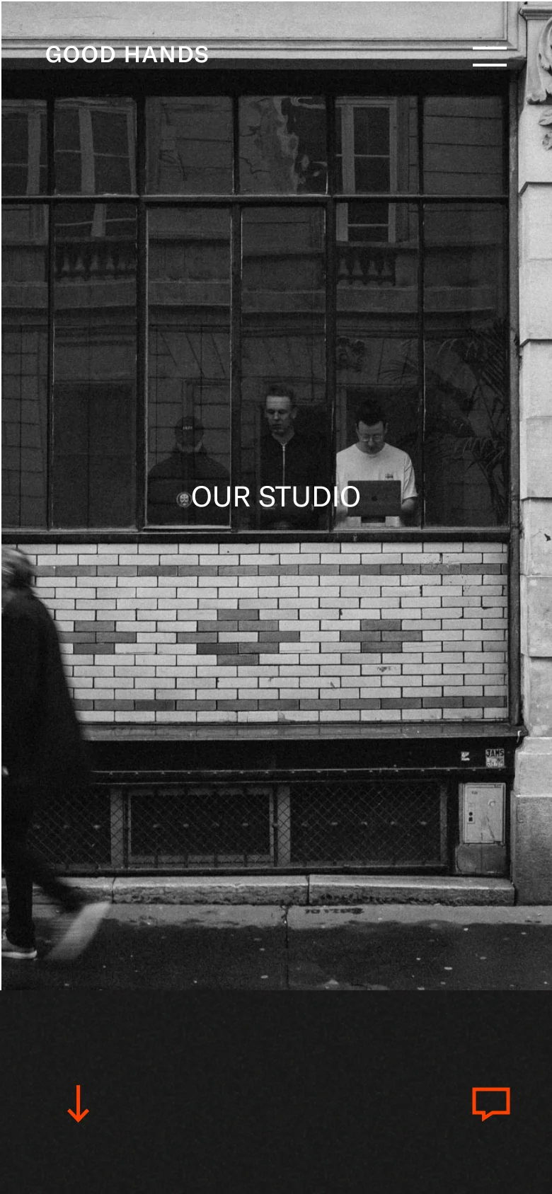 The mobile version simplifies the layout, focusing on a single large black and white photograph of a storefront window as the hero image. The text 'OUR STUDIO' is centered over the window, and the 'GOOD HANDS' logo and hamburger menu are positioned at the top. The design is vertically oriented with orange navigation icons at the bottom of the screen.