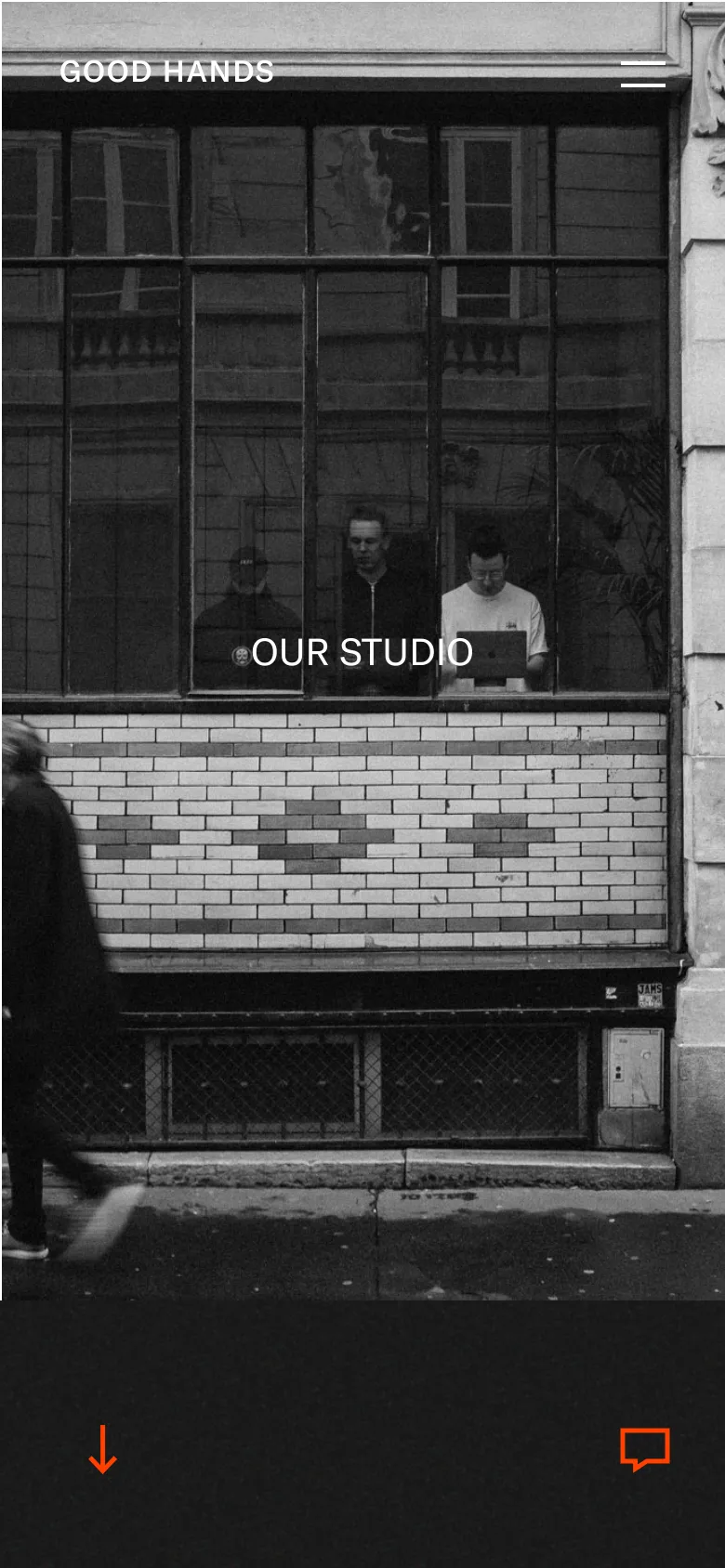 The mobile version simplifies the layout, focusing on a single large black and white photograph of a storefront window as the hero image. The text 'OUR STUDIO' is centered over the window, and the 'GOOD HANDS' logo and hamburger menu are positioned at the top. The design is vertically oriented with orange navigation icons at the bottom of the screen.