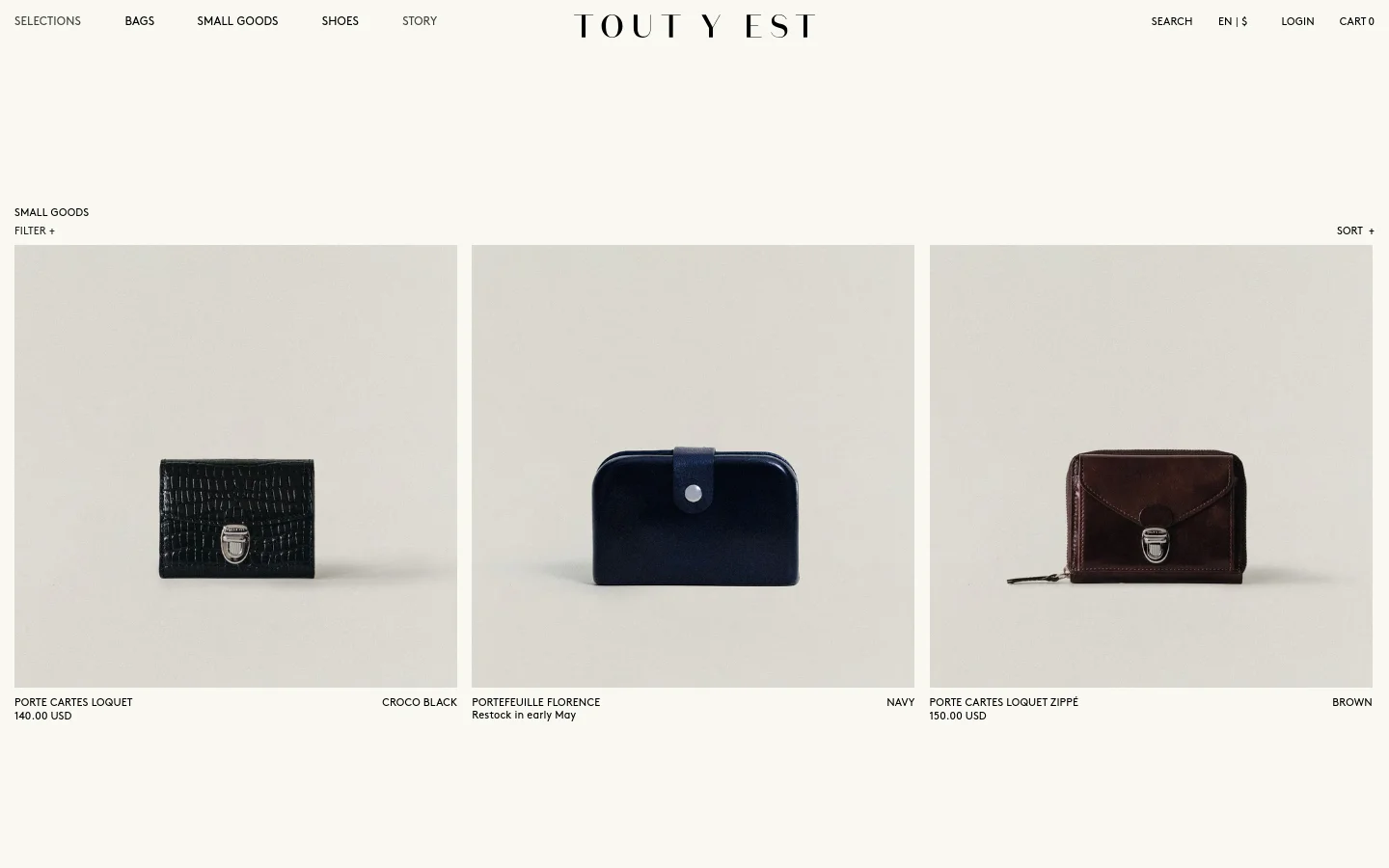 The desktop version of the Small Goods collection page features a minimalist design with a white background and black text. A top navigation bar includes links for Bags, Small Goods, Shoes, and Story, alongside a central brand logo. Below the header, a grid displays product images of wallets and cardholders against neutral backgrounds, with product names and prices listed underneath.
