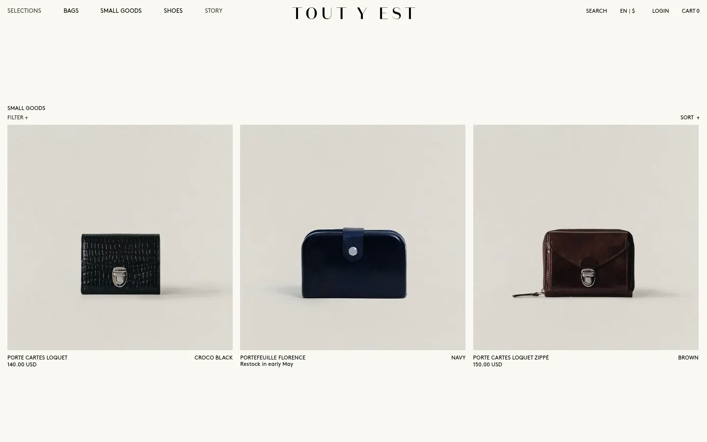 The desktop version of the Small Goods collection page features a minimalist design with a white background and black text. A top navigation bar includes links for Bags, Small Goods, Shoes, and Story, alongside a central brand logo. Below the header, a grid displays product images of wallets and cardholders against neutral backgrounds, with product names and prices listed underneath.