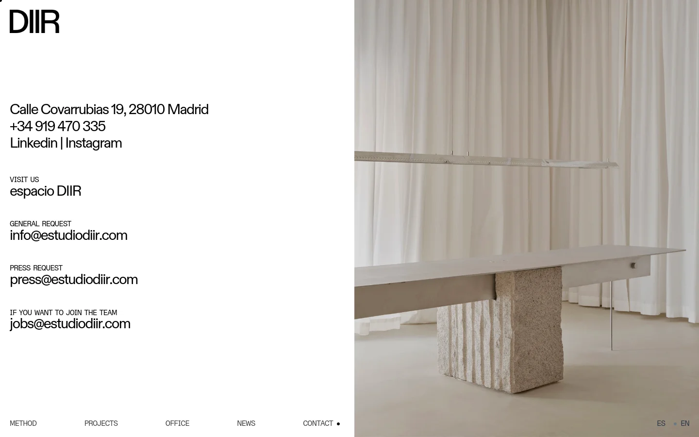 The contact page features a minimalist layout with black text on a white background. The left side contains the company logo, address, phone number, social links, and specific email addresses for general, press, and job inquiries. The right side displays a large, high-quality architectural photograph of a minimalist interior with white curtains and a stone-based table.