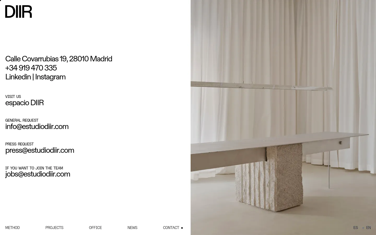 The contact page features a minimalist layout with black text on a white background. The left side contains the company logo, address, phone number, social links, and specific email addresses for general, press, and job inquiries. The right side displays a large, high-quality architectural photograph of a minimalist interior with white curtains and a stone-based table.
