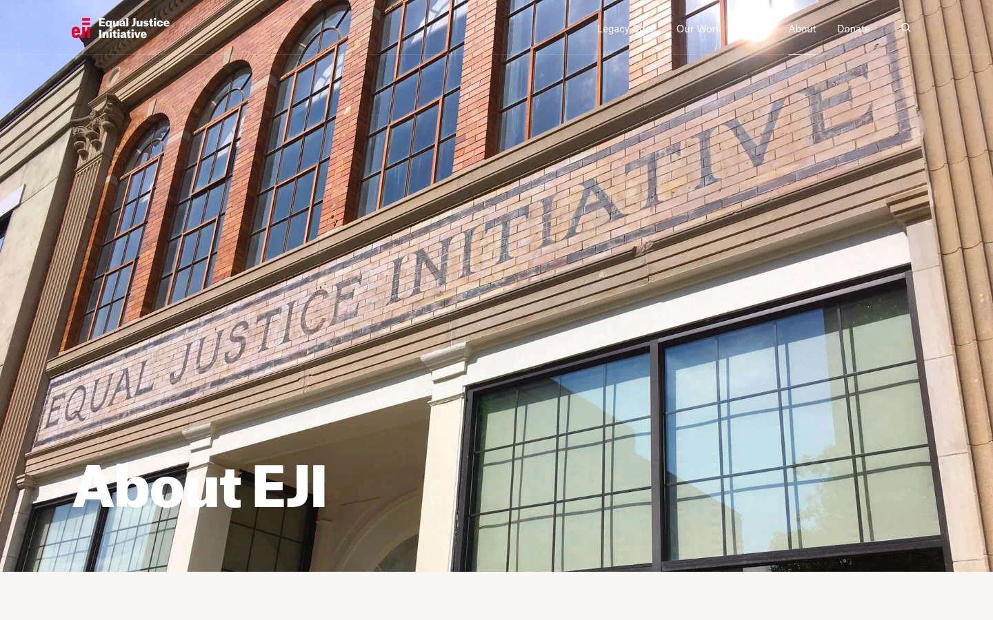 The desktop page features a large hero image of a brick building with 'EQUAL JUSTICE INITIATIVE' inscribed in large letters across the facade, overlaid with the headline 'About EJI'. A white navigation bar at the top includes the EJI logo and links for Legacy Sites, Our Work, About, Donate, and a search icon. The layout is clean with a focus on the architectural imagery and bold typography.