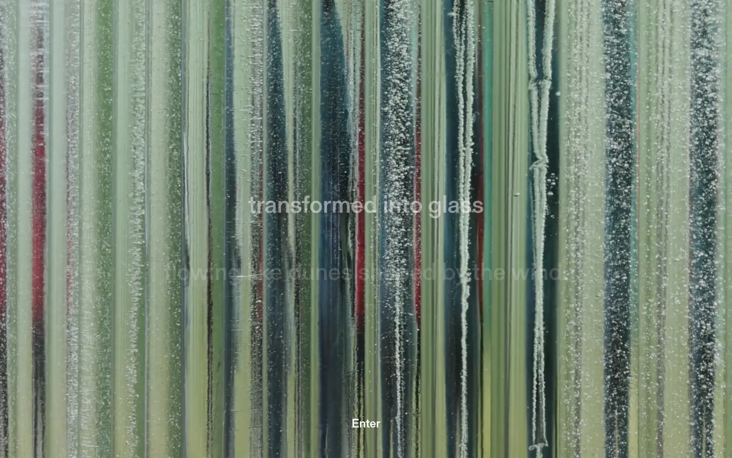 The desktop homepage features a full-screen, high-resolution background image of vertical glass pillars with varying shades of green, blue, and subtle red. Centered white text reads 'transformed into glass' above an 'Enter' call to action button, set against the textured, light-refracting glass columns.