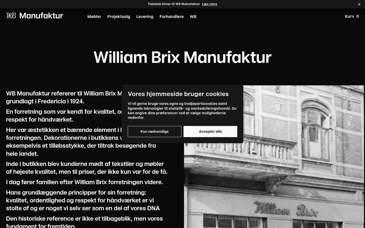 The desktop page features a dark theme with a large white headline 'William Brix Manufaktur' set against a black background. A large hero image showing a vintage storefront is partially visible on the right, while text content is aligned to the left. A cookie consent overlay is centered on the screen with two buttons: 'Kun nødvendige' and 'Accepter alle'.