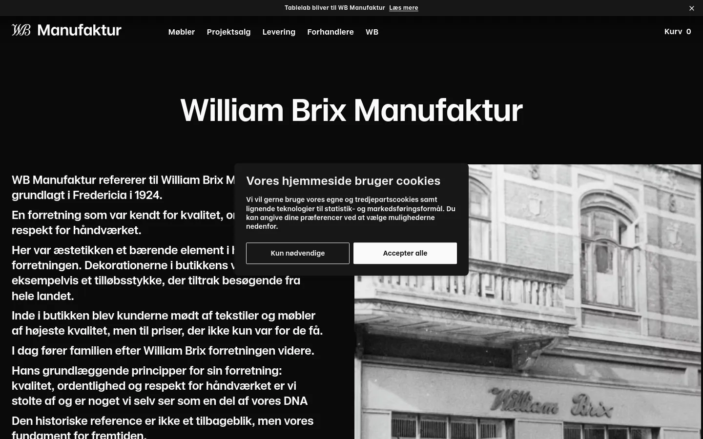 The desktop page features a dark theme with a large white headline 'William Brix Manufaktur' set against a black background. A large hero image showing a vintage storefront is partially visible on the right, while text content is aligned to the left. A cookie consent overlay is centered on the screen with two buttons: 'Kun nødvendige' and 'Accepter alle'.