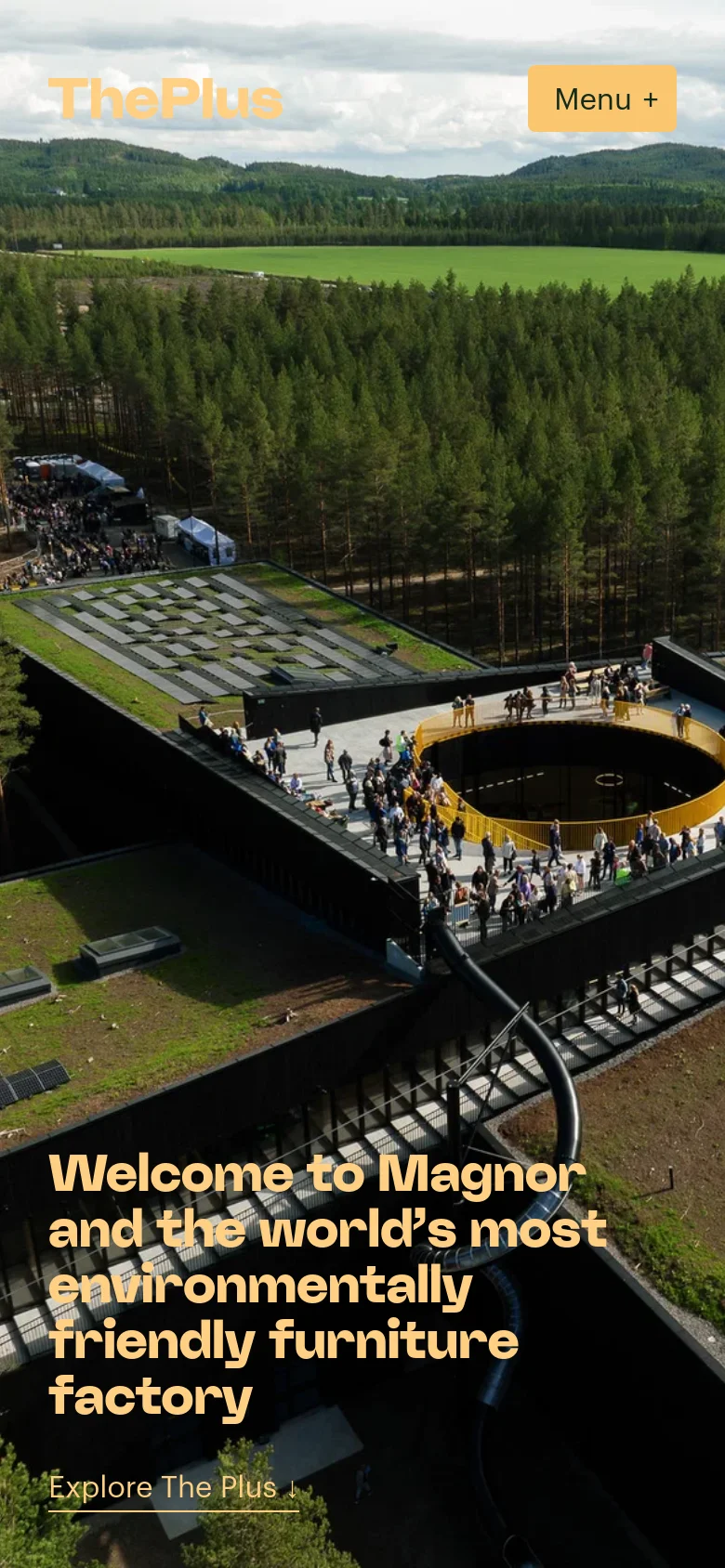 The mobile version presents a vertically oriented aerial view of the sustainable factory and forest, with the 'ThePlus' logo and a 'Menu +' button at the top. The headline 'Welcome to Magnor and the world’s most environmentally friendly furniture factory' is centered in bold white text. A single 'Explore The Plus' call to action is positioned at the bottom of the hero section.