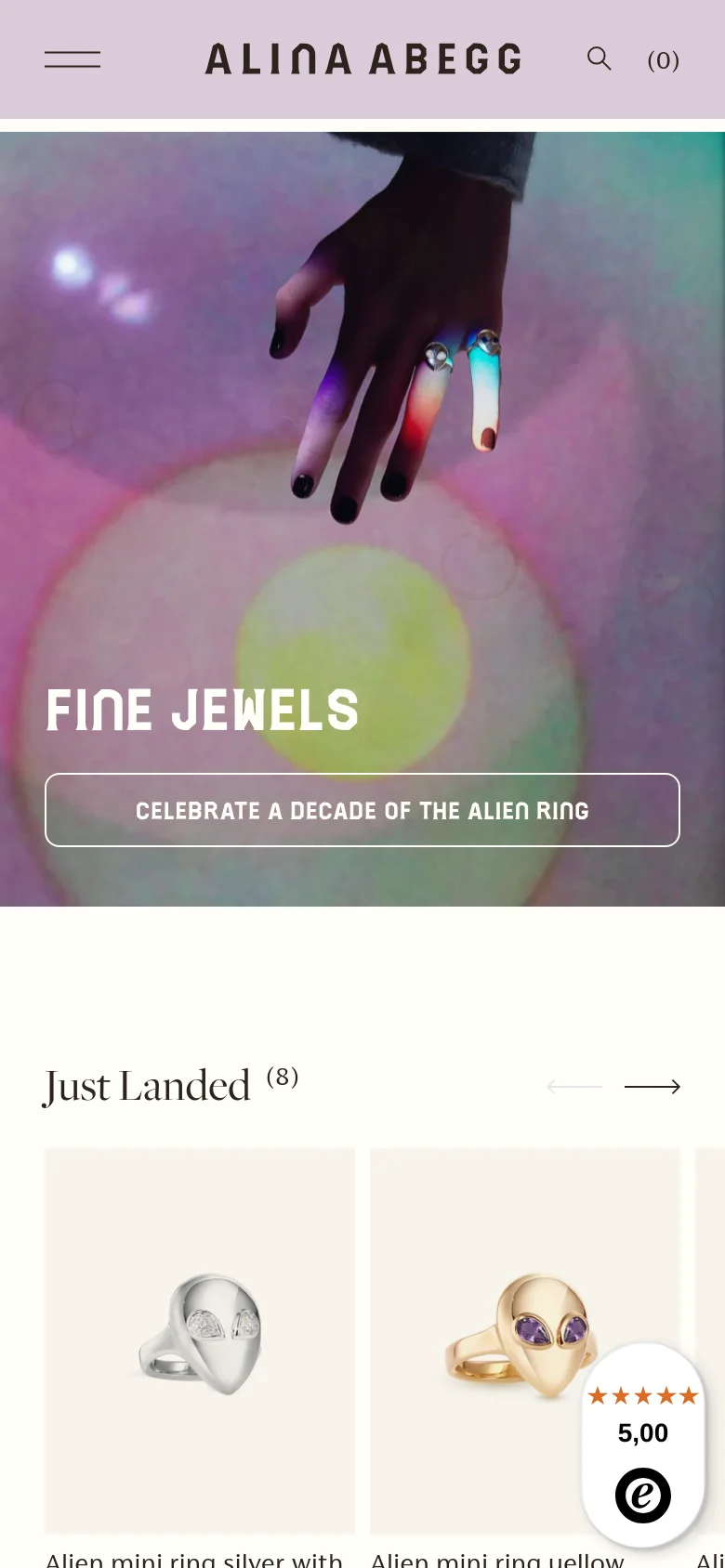 The mobile version presents a vertically stacked layout starting with the iridescent hero image and 'FINE JEWELS' text. Below the hero section, the 'Just Landed' product section displays jewelry items in a single-column or smaller grid format, optimized for vertical scrolling. The navigation bar remains at the top with a hamburger menu, brand name, search icon, and cart count.
