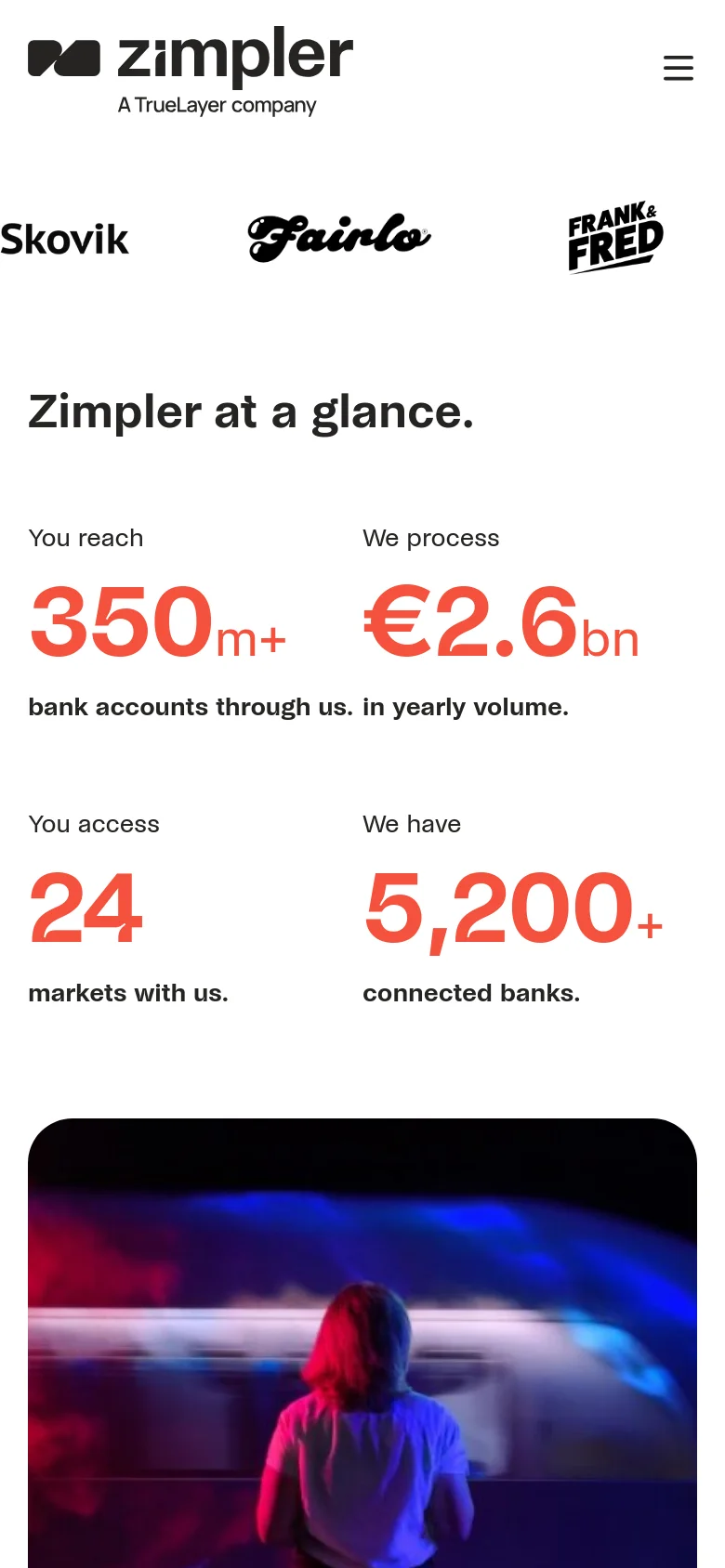 The mobile version uses a simplified layout with a hamburger menu icon in the top right and the Zimpler logo centered. The hero section and statistics are stacked vertically to fit the narrow screen, maintaining the white background and large orange numbers for key metrics like '24 markets' and '5,200+ connected banks.' The primary navigation is hidden behind the menu icon to prioritize content visibility.