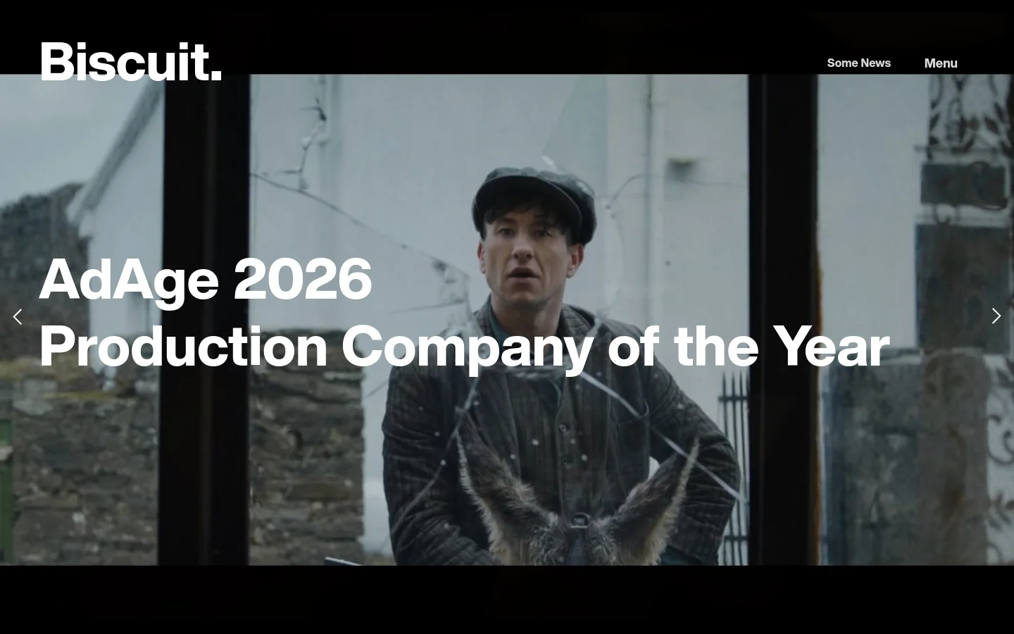 The desktop News page features a minimalist design with a large hero image slider showcasing film production stills. A prominent headline 'AdAge 2026 Production Company of the Year' is overlaid on a cinematic shot of a man in a cap, with navigation arrows on the sides and the 'Biscuit.' logo in the top left corner.