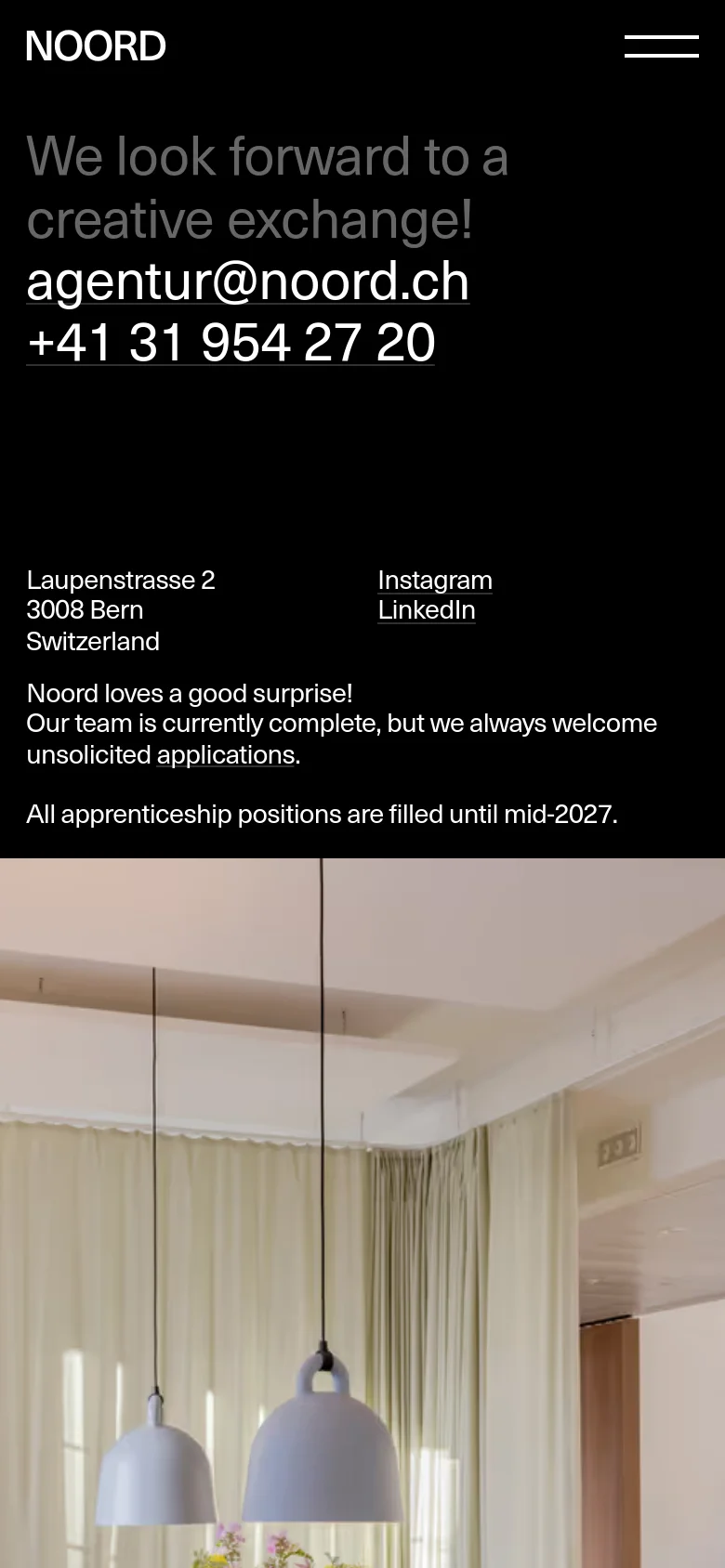 The mobile version maintains the dark aesthetic and large typography but stacks the content vertically. The contact details and address appear in a single column, followed by social links and the application text. The large lifestyle image remains at the bottom of the viewport.