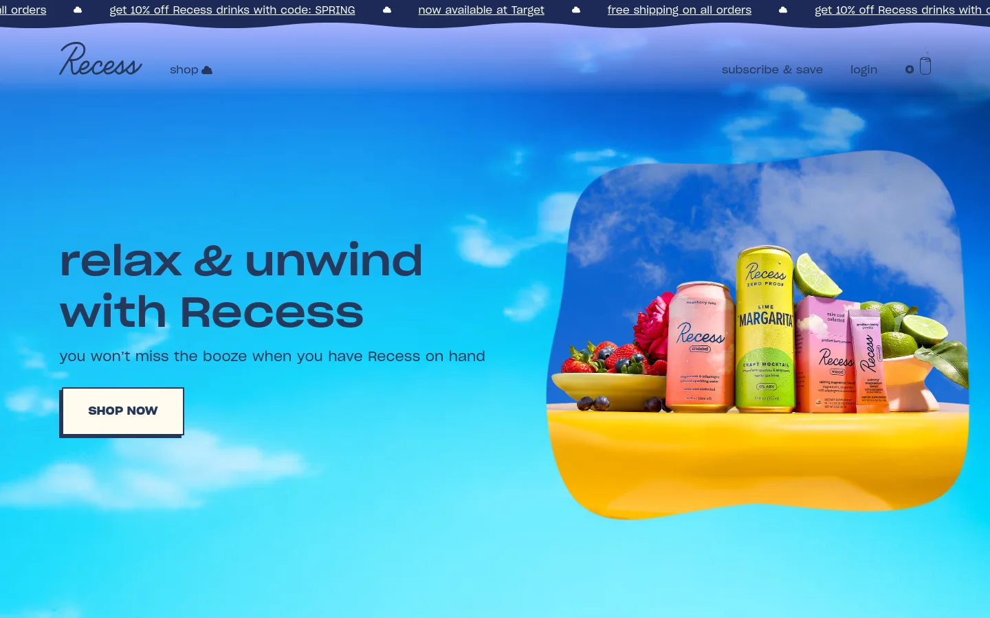 The desktop homepage features a wide hero section with a bright blue sky background and white clouds. On the left, the headline 'relax & unwind with Recess' is displayed above a 'SHOP NOW' button, while the right side shows Recess beverage cans and powders arranged on a yellow surface with fresh fruit. A navigation bar at the top includes the Recess logo, shop link, and account options.