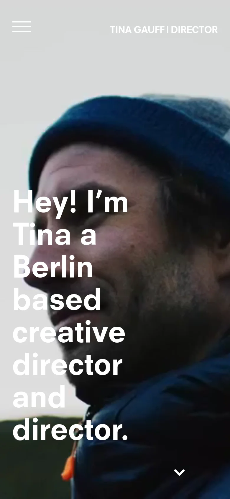 The mobile version displays a vertically oriented hero image of a person in a blue beanie, with the same large white headline text stacked vertically. The navigation is condensed into a hamburger menu icon on the top left, and a downward arrow icon is centered at the bottom to indicate more content below.