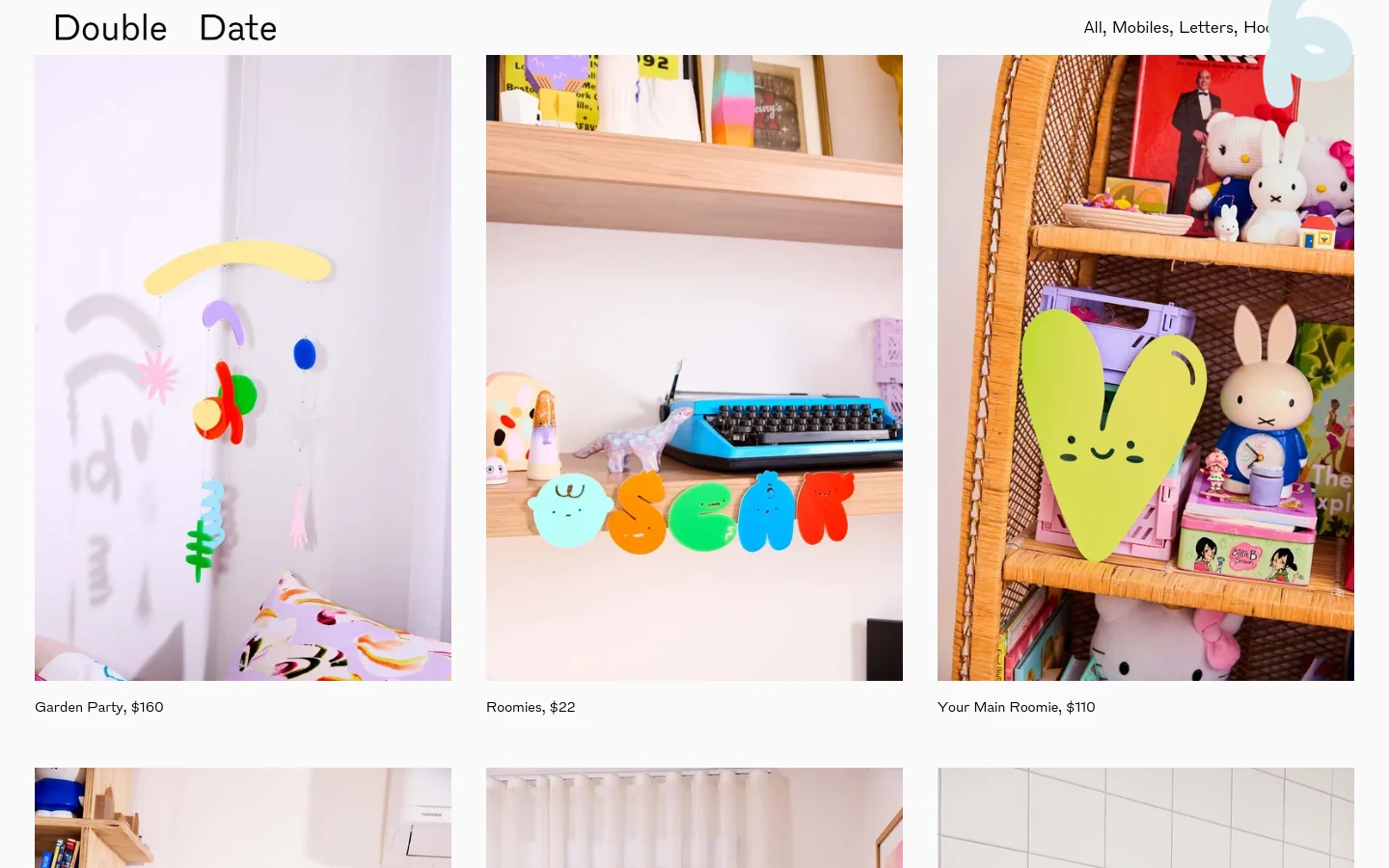 The Double Date homepage features a clean, minimalist layout with a white background and black text. A grid of large, colorful product images showcases handmade hanging mobiles, such as the Garden Party and Roomies, each accompanied by its name and price. The desktop view displays three products side-by-side in a single row.