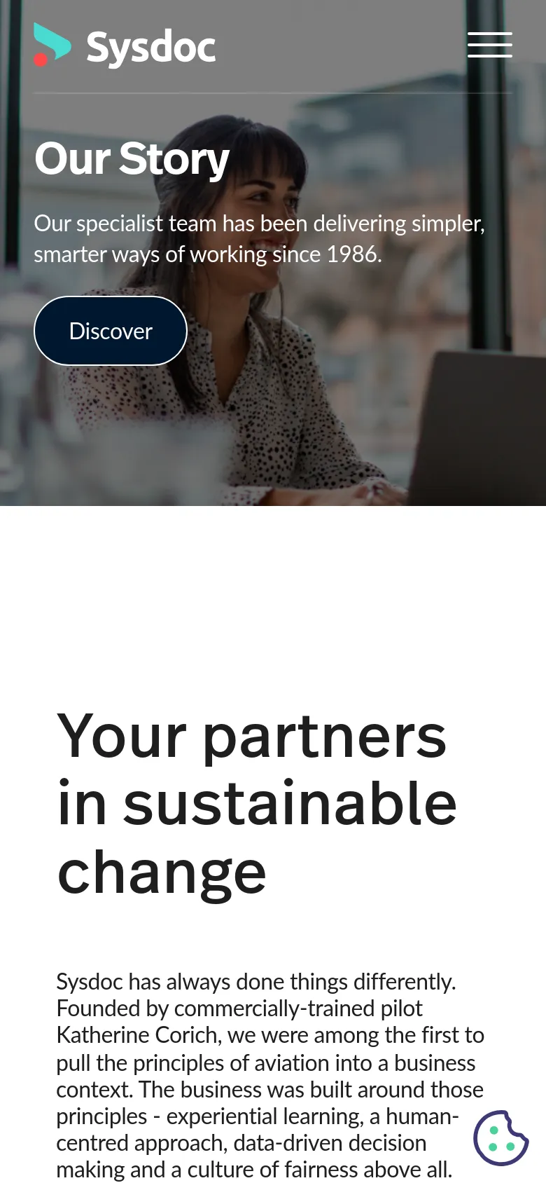 The mobile version presents a vertically stacked layout with the Sysdoc logo and a hamburger menu icon at the top. The hero section displays the 'Our Story' headline and subheadline over the same office imagery, with a large, outlined 'Discover' button centered below the text. The layout is simplified for a narrow screen, focusing on high-contrast text and large touch targets.