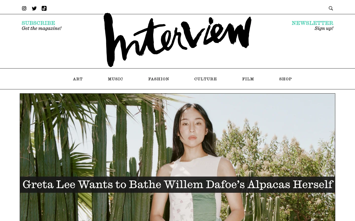 The Interview Magazine homepage features a large hero image of Greta Lee against a backdrop of cacti, with a bold headline overlay. Below the hero section, a grid layout displays various articles with square thumbnails, category labels, headlines, and author names. The design uses a clean white background with black typography and teal accents for 'Subscribe' and 'Newsletter' links.