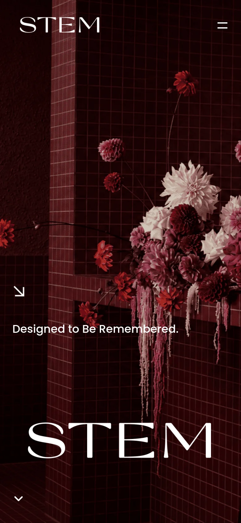 The mobile version simplifies the layout, replacing the horizontal navigation menu with a hamburger icon in the top right. The hero image remains a dark, red-toned floral arrangement, and the large 'STEM' text and 'Designed to Be Remembered' tagline are centered vertically. A downward arrow at the bottom indicates more content below.