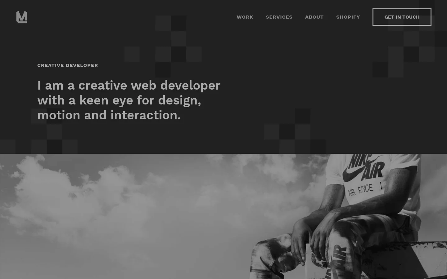 The desktop landing page features a dark, minimalist design with a large headline stating, 'I am a creative web developer with a keen eye for design, motion and interaction.' A navigation bar at the top includes links for Work, Services, About, Shopify, and a 'Get In Touch' button. Below the hero text, a large black and white photograph shows a person sitting on a ledge overlooking a city skyline.