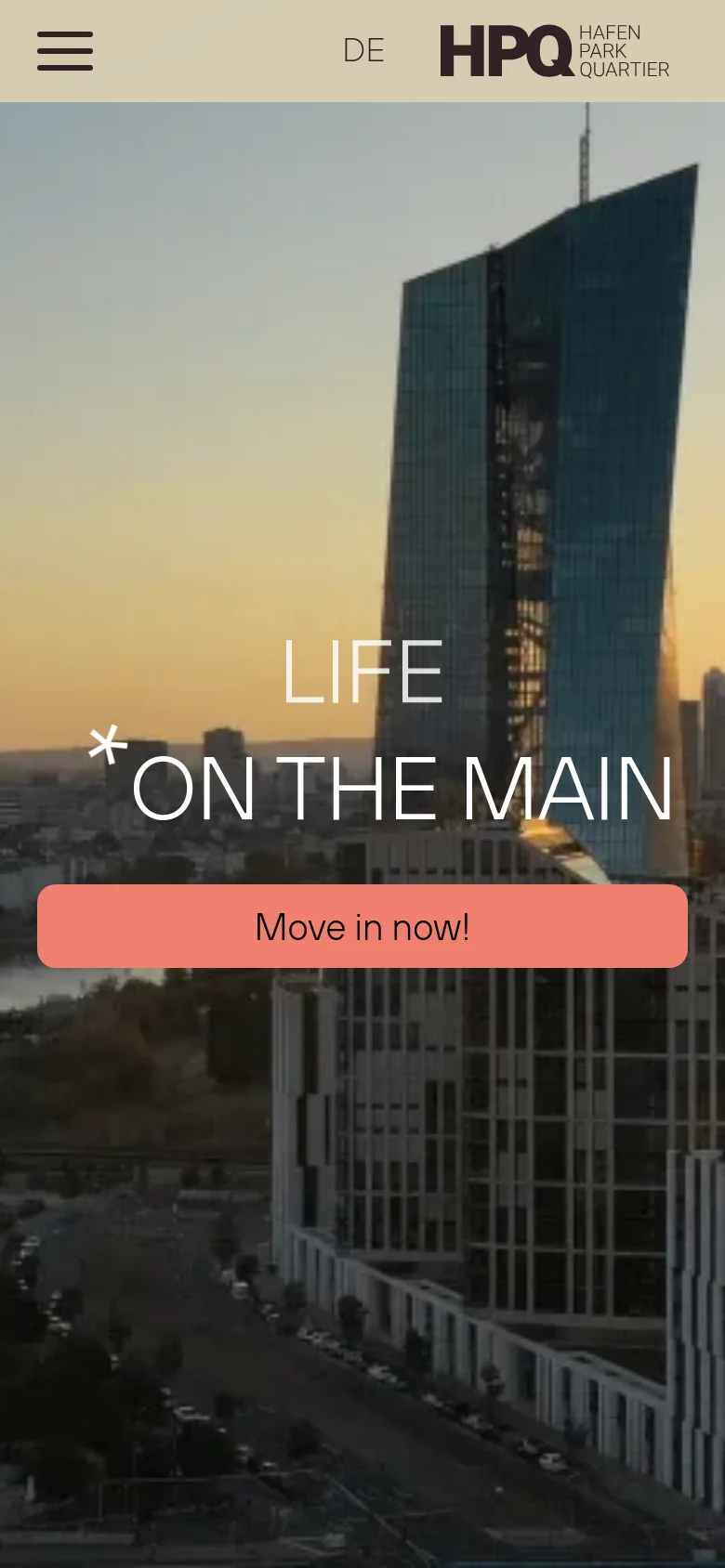 Mobile view of the homepage showing a vertically oriented hero image of a skyscraper at dusk. The headline 'LIFE * ON THE MAIN' is centered over the image, followed by a large, prominent salmon-colored 'Move in now!' call-to-action button. A hamburger menu and language selector are visible at the top.