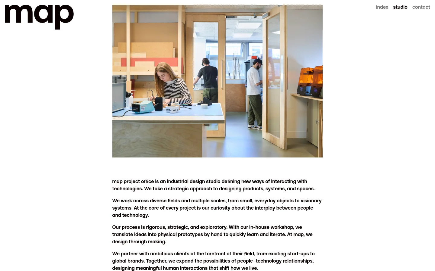 The desktop page features a minimalist design with a large 'map' logo on the left and navigation links on the right. A large hero image shows a bright, modern industrial design studio with designers working at wooden benches, followed by several paragraphs of descriptive text about the studio's mission and process.