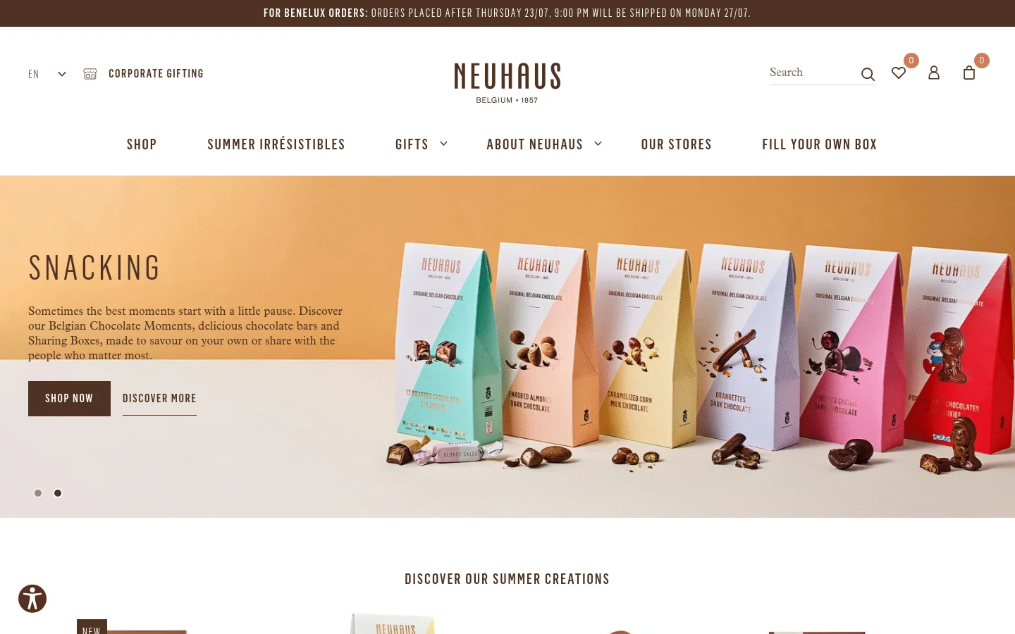 The desktop homepage features a clean, elegant layout with a white background and gold accents. A large hero banner showcases various colorful Neuhaus chocolate snack boxes against a warm orange background, accompanied by the headline 'SNACKING' and 'Shop Now' and 'Discover More' buttons. The top navigation includes links for Shop, Summer Irrésistibles, Gifts, About Neuhaus, Our Stores, and Fill Your Own Box.