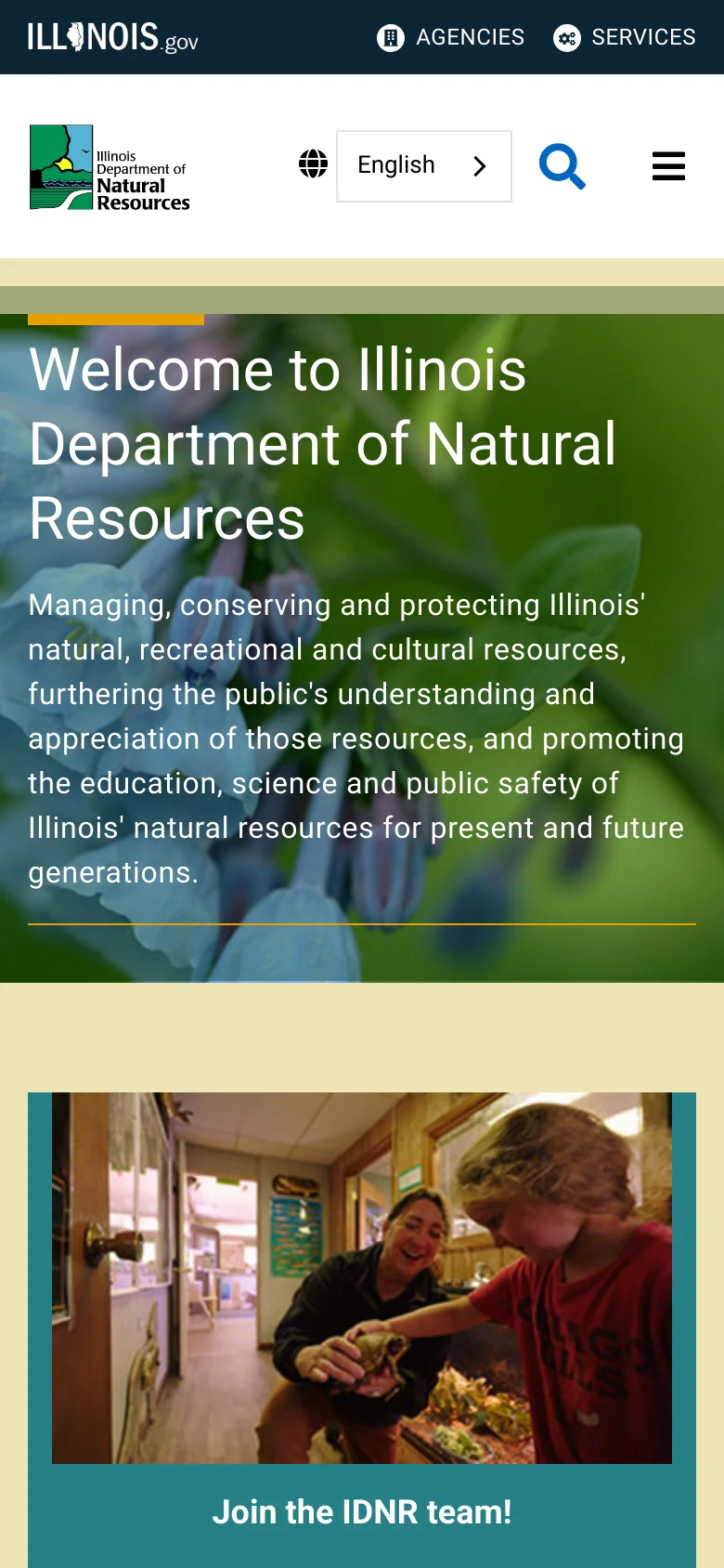 The mobile version presents a simplified layout with a condensed header featuring the agency logo, a language selector, a search icon, and a hamburger menu icon for navigation. The hero section remains prominent, displaying the large welcome headline and mission text over the blue flower imagery. The top Illinois.gov utility bar is minimized to focus on mobile-friendly touch targets.