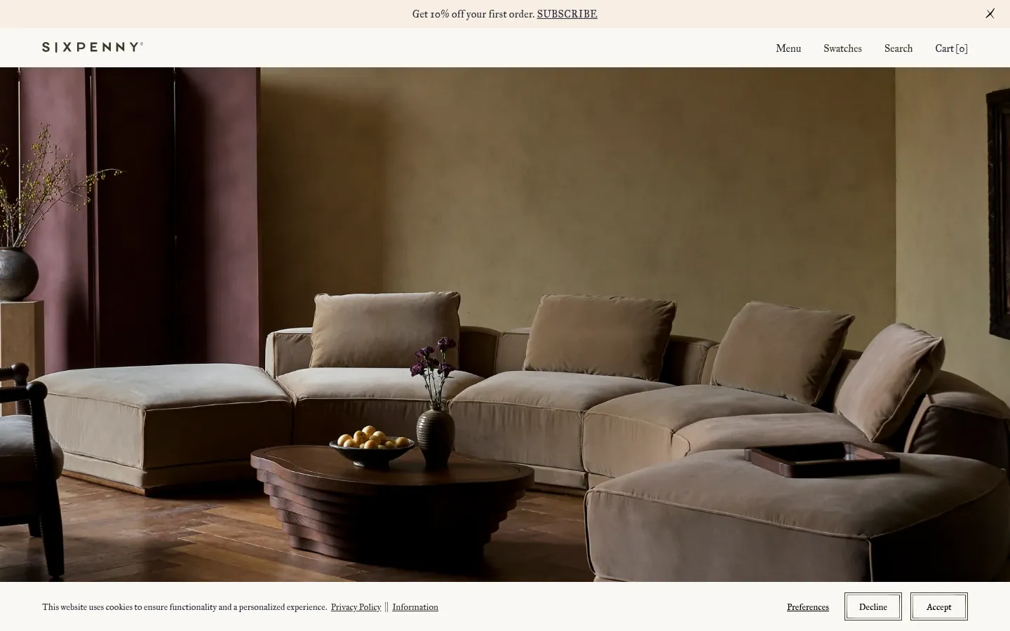 The desktop homepage features a minimalist navigation bar with links for Menu, Swatches, Search, and Cart. The hero section displays a large, high-quality lifestyle photograph of a beige modular sofa in a warm, earth-toned room with a dark wooden coffee table. A thin promotional banner at the top offers 10% off with a subscribe link.