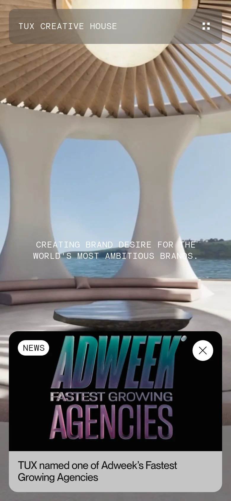 The mobile version transitions to a full-screen hero image of a modern, white architectural structure overlooking the ocean. The layout is vertically oriented with the agency name and navigation condensed, and the Adweek news announcement appears as a large overlay at the bottom of the screen.