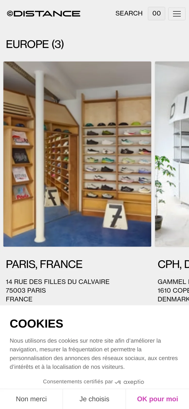 The mobile version presents a single-column vertical layout where store images and location details are stacked. The navigation is condensed into a hamburger menu and a search icon at the top, and the cookie consent banner spans the bottom of the screen.