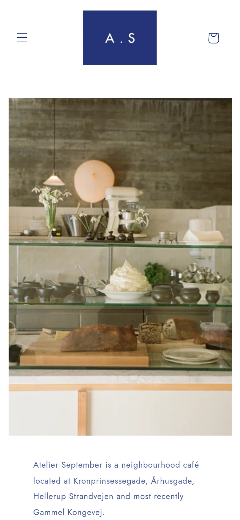 The mobile version simplifies the layout, replacing the full navigation menu with a hamburger icon and a shopping bag icon next to a centered 'A.S' logo. The content remains vertically stacked, starting with the hero image of the cafe display case followed by the introductory text and cookbook promotion.