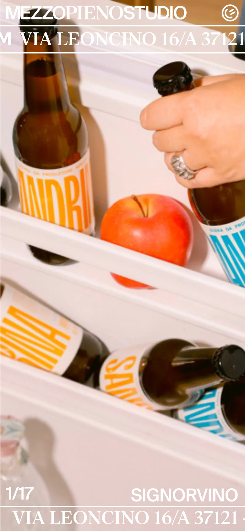 The mobile version presents a single, vertically oriented close-up image of hands interacting with beer bottles and an apple on a white shelf. The layout is simplified, with the studio name and contact details like the address and email overlaid in large white typography across the center and bottom of the screen.