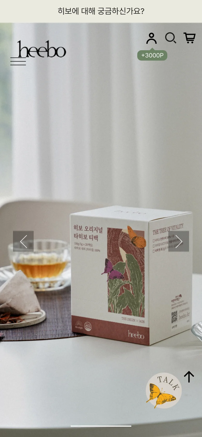 The mobile version shows a full-screen hero image of a Heebo tea box on a white table next to a cup of tea. The layout is vertically oriented with a minimalist header containing the logo, menu, and icons, and a circular 'TALK' button with a butterfly graphic at the bottom right.