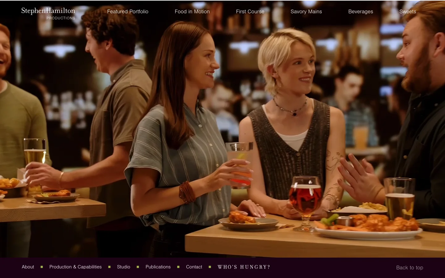 The desktop homepage features a large, cinematic hero video of people socializing and enjoying drinks in a warm, dimly lit restaurant setting. Below the video, a grid of high-quality, vibrant food photography displays various dishes like pasta, salads, and seafood. A dark navigation bar at the top includes links for 'Featured Portfolio', 'Food in Motion', and food categories, while a footer contains links for 'About', 'Studio', and 'Contact'.