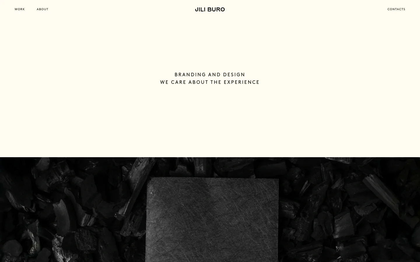 The desktop homepage features a minimalist design with a cream background and black text. A large hero section displays the headline 'BRANDING AND DESIGN' followed by 'WE CARE ABOUT THE EXPERIENCE', positioned above a dark, textured close-up image of charcoal. Navigation links for 'WORK', 'ABOUT', and 'CONTACTS' are spread across the top header with the 'JILI BURO' logo centered.