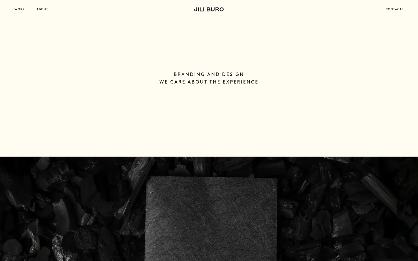 The desktop homepage features a minimalist design with a cream background and black text. A large hero section displays the headline 'BRANDING AND DESIGN' followed by 'WE CARE ABOUT THE EXPERIENCE', positioned above a dark, textured close-up image of charcoal. Navigation links for 'WORK', 'ABOUT', and 'CONTACTS' are spread across the top header with the 'JILI BURO' logo centered.