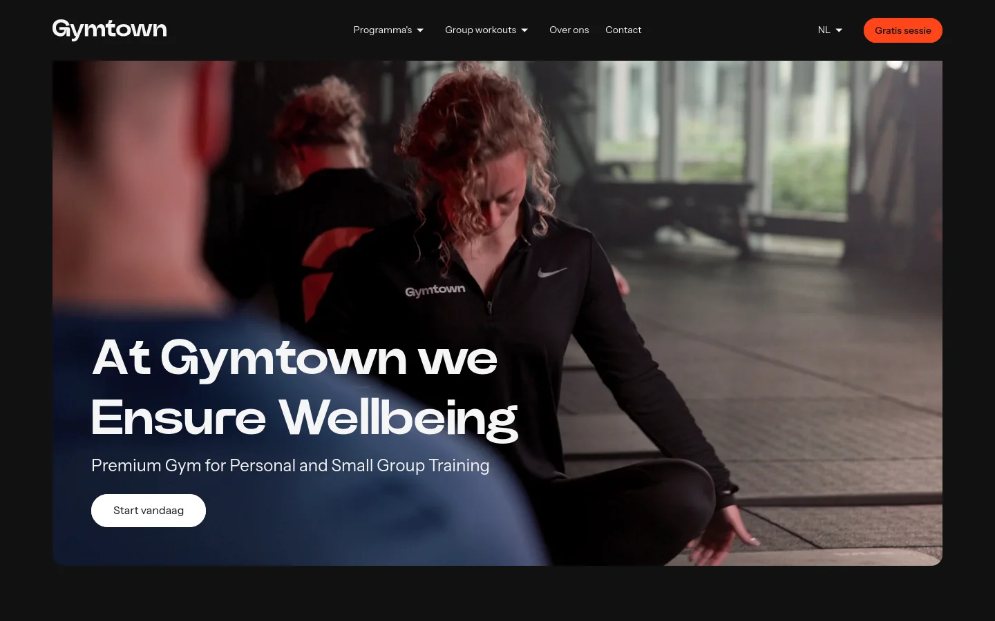 The desktop homepage features a dark theme with a large hero image of people training in a gym. The headline 'At Gymtown we Ensure Wellbeing' is overlaid on the image next to a white 'Start vandaag' call-to-action button, with a navigation menu at the top containing links for programs, workouts, and contact info.