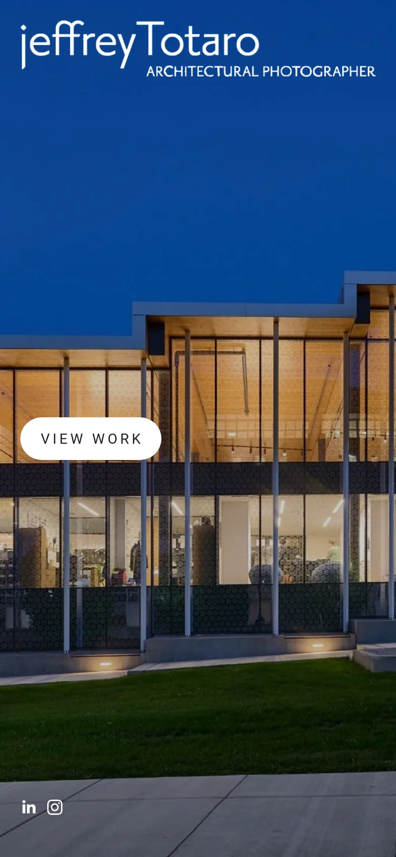 The mobile version presents a vertically oriented hero image of a modern building with large glass windows illuminated from within at dusk. The branding and 'VIEW WORK' button are centered, and social media icons are located at the bottom left, maintaining the minimalist white-on-dark aesthetic.
