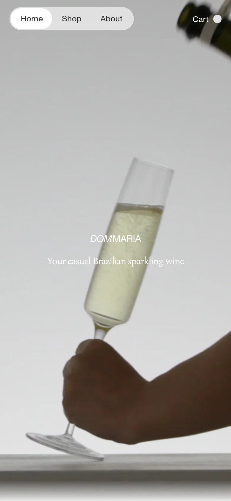 The mobile version presents a vertically oriented hero image of the champagne glass and bottle, with the brand name and tagline centered in the middle of the screen. The navigation is simplified, showing 'Home', 'Shop', and 'About' in a large white pill-shaped button on the left, and 'Cart' on the right.